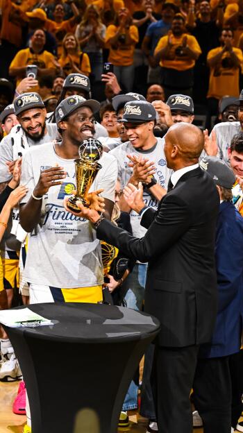 Photo of Indiana Pacers players, including Pascal Siakam, celebrating an NBA basketball Finals victory, holding the championship trophy amidst cheering fans.