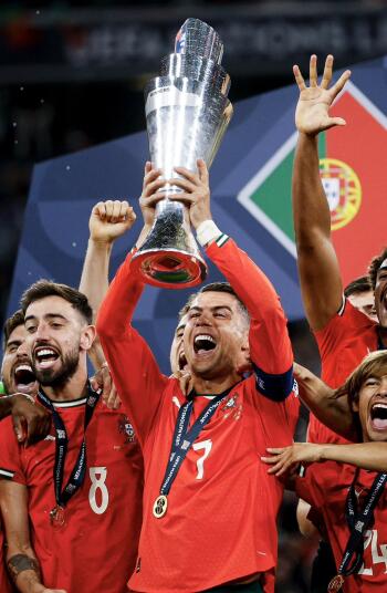 Portugal National Football Team players, including Cristiano Ronaldo and Bruno Fernandes, celebrate winning a soccer trophy, with Ronaldo lifting the cup in triumph.