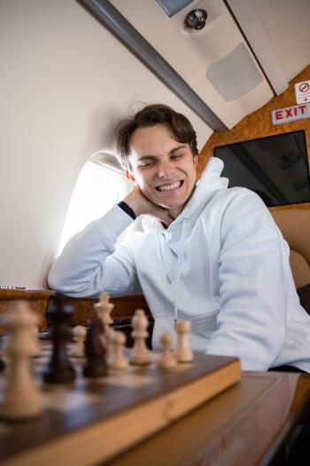 Phone wallpaper featuring Oscar Piastri smiling while sitting on a plane with a chessboard in the foreground, compatible with both iPhone and Android devices.