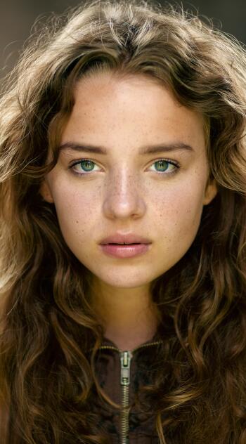 Close-up portrait of actress Bo Bragason with green eyes, natural freckles, and wavy brown hair, designed as a phone wallpaper compatible with iPhones and Android devices.