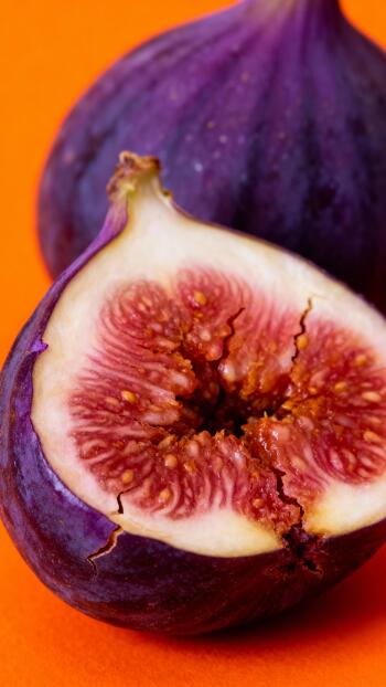 Close-up of a halved purple fig against a bright orange background, vertical phone wallpaper for iPhones and Android phones.