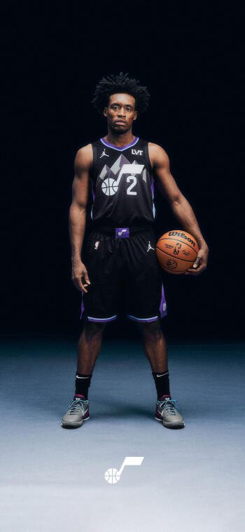 Vertical phone wallpaper of an NBA guard in a black Utah Jazz jersey (#2) standing centered, holding a basketball against a dark studio background.