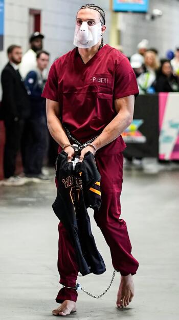 Phone wallpaper: an NFL player arriving at the Super Bowl barefoot in maroon scrubs and a face shield, hands chained while holding a game jersey.