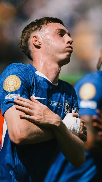 Phone wallpaper of a Chelsea F.C. player in blue kit celebrating, arms crossed over his chest, close-up with a blurred stadium crowd in the background.