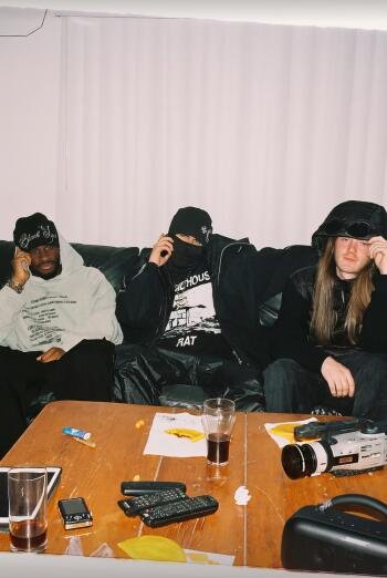 Phone wallpaper of three hooded musicians lounging on a couch with a rapper/music vibe; tagged EsDeeKid.