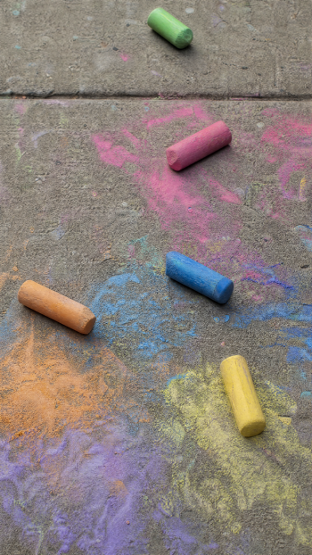 iPhone wallpaper of colorful sidewalk chalk sticks and smeared pastel art on a concrete sidewalk.
