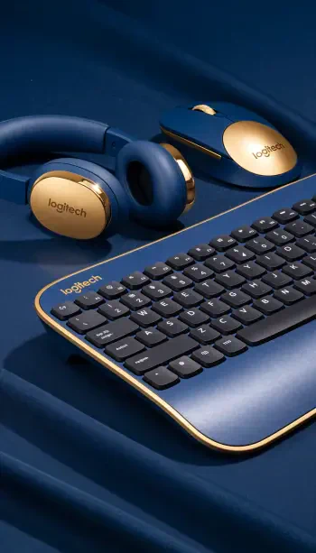 iPhone wallpaper showing navy-and-gold Logitech keyboard, wireless mouse, and over-ear headphones arranged on blue silk.