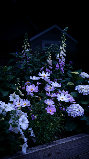 iPhone wallpaper showing a garden flower bed with pale purple and white flowers clustered against deep evening foliage and a dim house silhouette in the background.