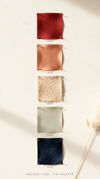 iPhone wallpaper showing a vertical color palette of five fabric swatch samples—red, copper, cream, sage, navy—pinned on a textured white wall with a dried flower accent.