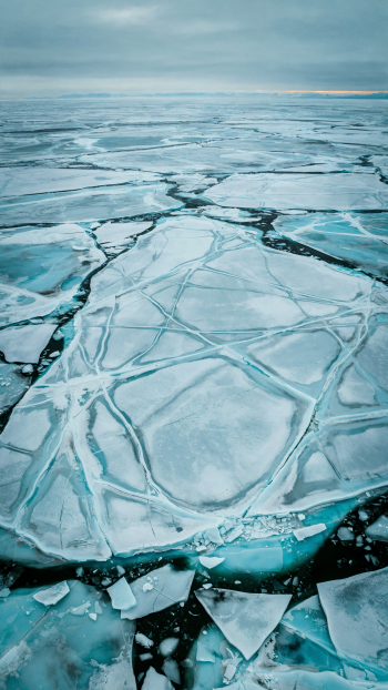 Vertical iPhone wallpaper of cracked sea ice—frozen turquoise plates and dark leads stretching to a pale winter horizon.