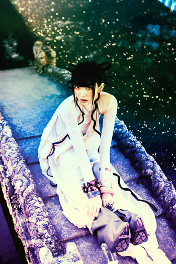 Woman cosplayer in a What a Wonderful Life costume seated on a stone bridge with sparkling bokeh, framed as a vertical iPhone wallpaper.