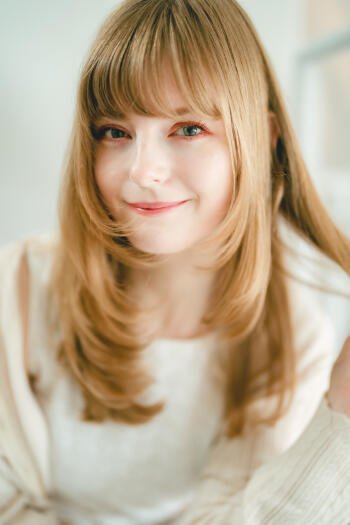 Soft-lit close-up portrait of a smiling blonde model, warm photography/camera tones, styled as a phone/iPhone wallpaper.