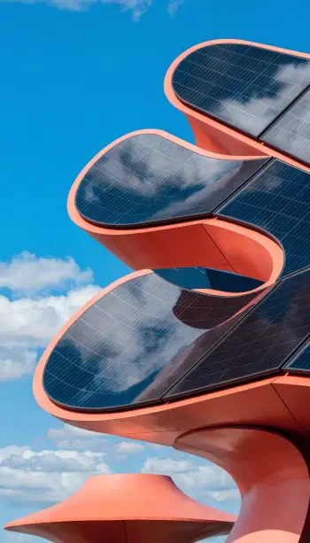 Vertical phone wallpaper: futuristic coral-red building with curving platforms covered in reflective solar panels against a blue sky.