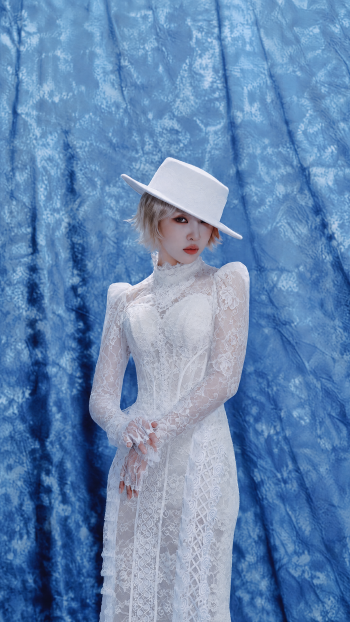 iPhone wallpaper: woman in a white lace dress and wide-brimmed white hat posed against a blue textured backdrop, styled with the word CALLING.