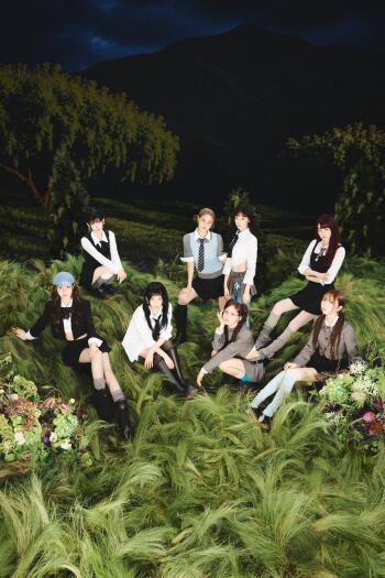 iPhone wallpaper portrait of a female pop group in a Sour Grapes concept: eight women in school-style outfits sitting on lush grass beneath a moody night sky.