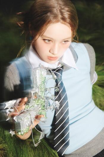 Phone wallpaper of a schoolgirl in uniform and striped tie, reaching with crumpled foil-wrapped green candy — moody 'Sour Grapes' pop-concept vibe.