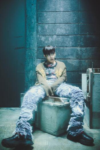 ATEEZ Hongjoong Golden Hour phone wallpaper portrait, seated in distressed denim against a moody blue industrial wall.