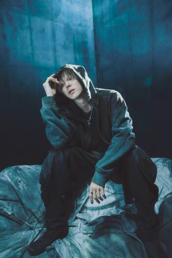 ATEEZ Yunho in a dark hoodie, seated against a moody blue backdrop in this Golden Hour phone wallpaper.