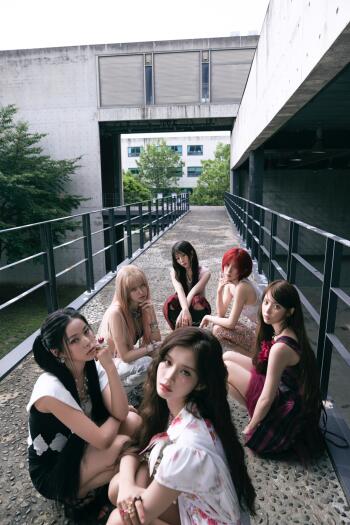 NMIXX Strange Muse fashion group portrait of six women seated on an outdoor walkway, vertical iPhone wallpaper.