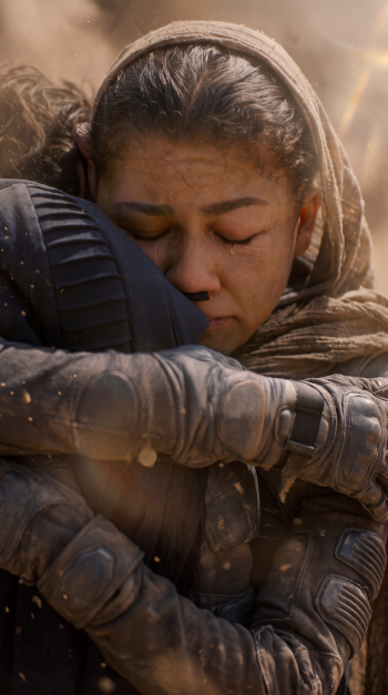 Zendaya embraces a fellow traveler in a tender Dune: Part Three scene, shown as a cinematic iPhone wallpaper.