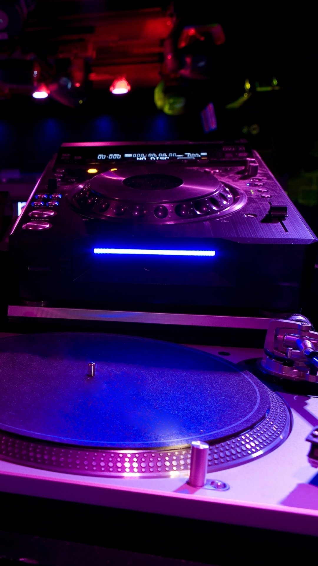 Colorful phone wallpaper of a DJ setup: close-up turntable and mixer glowing under neon club lights with vivid purple and blue highlights.