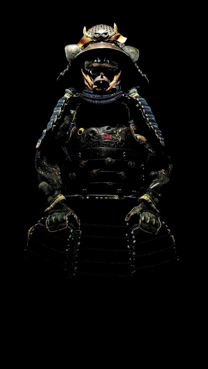 Phone wallpaper photography of a samurai in full traditional armor, low-key lighting highlighting the helmet and chest plate against a deep black background.