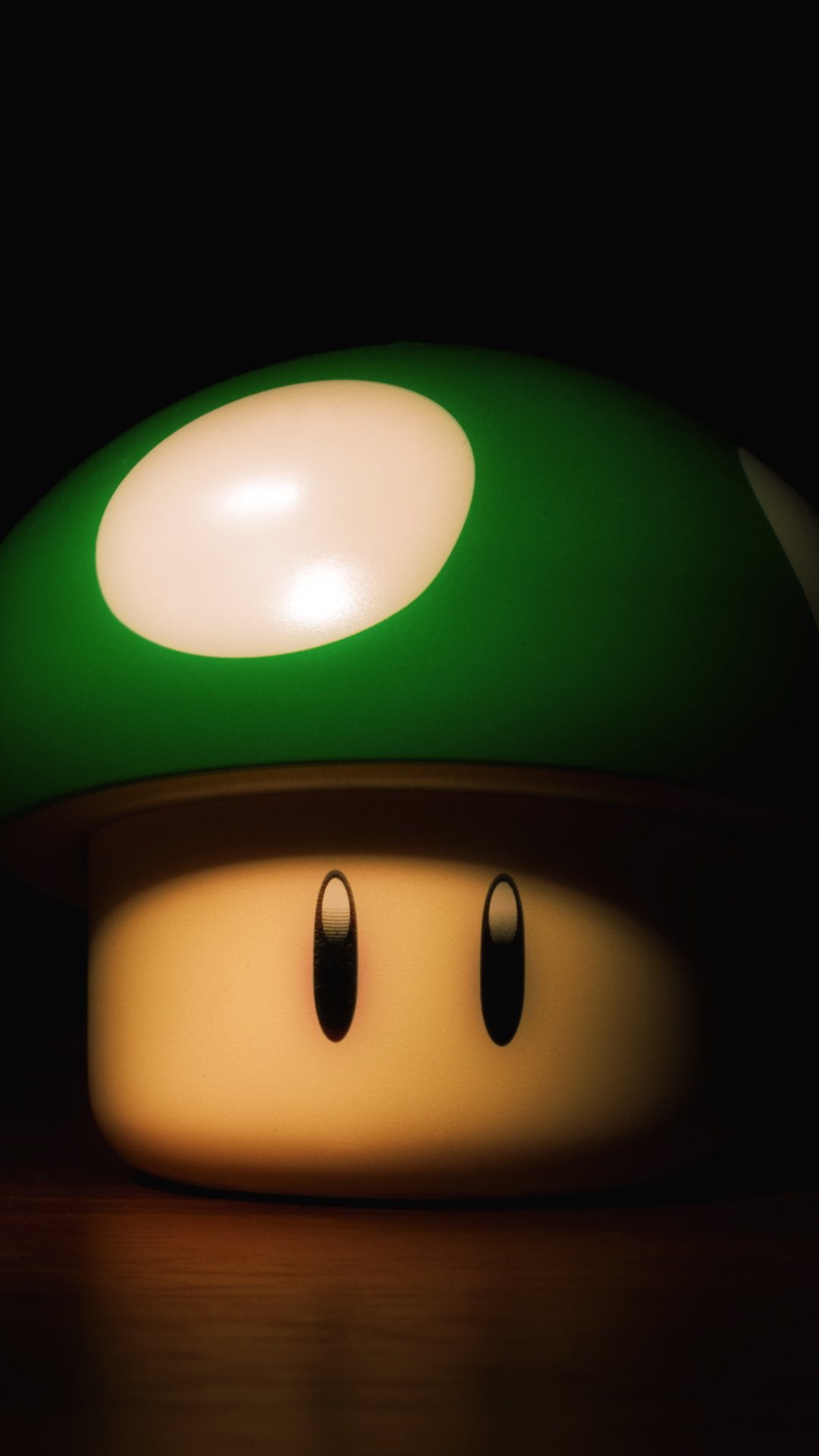 Phone wallpaper showing a close-up of Mario's green 1-Up mushroom with glossy white spots, warm lighting and a deep black background.