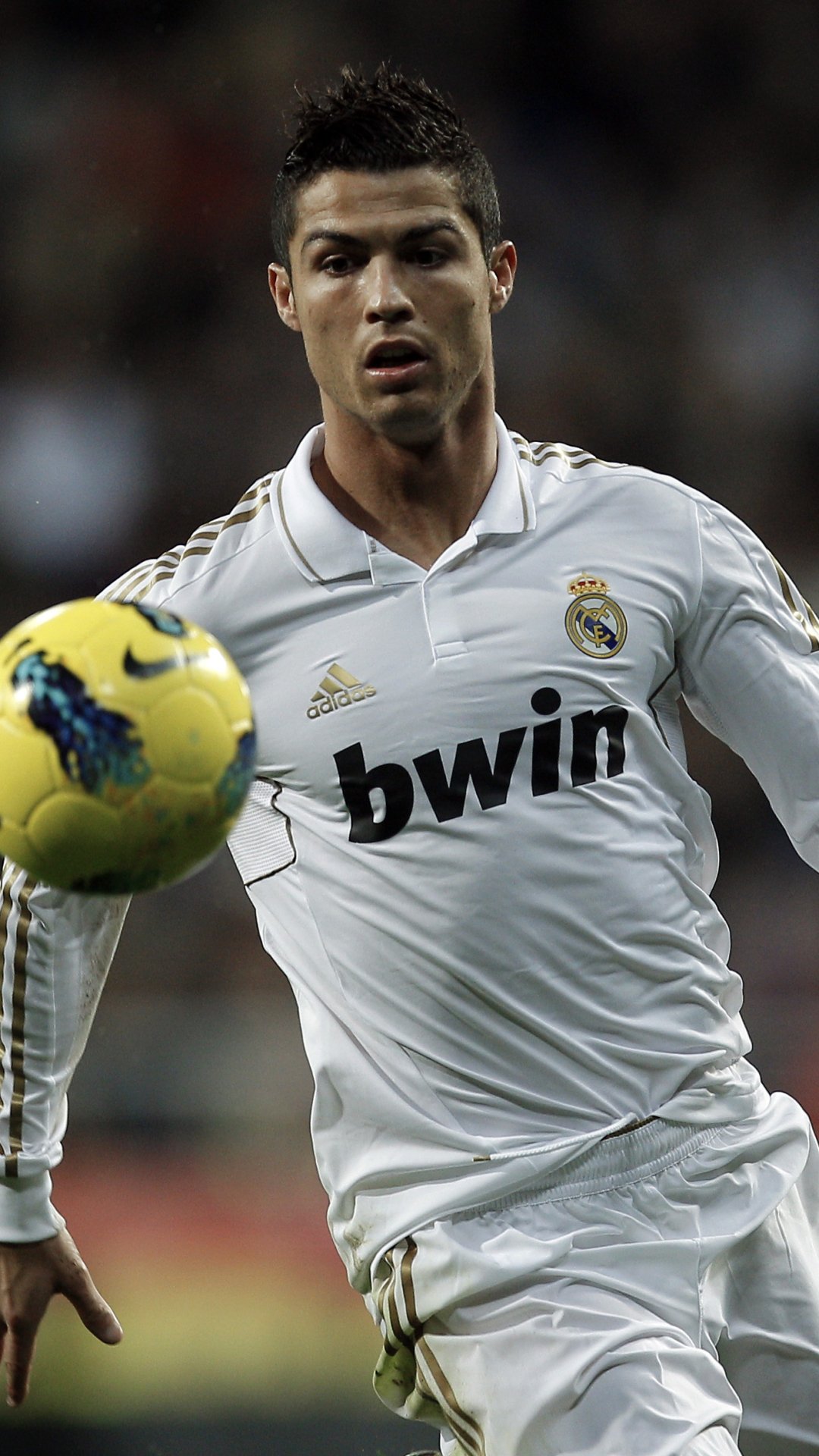 Phone wallpaper featuring Cristiano Ronaldo in Real Madrid C.F. white kit, focused on controlling a yellow soccer ball during a match.