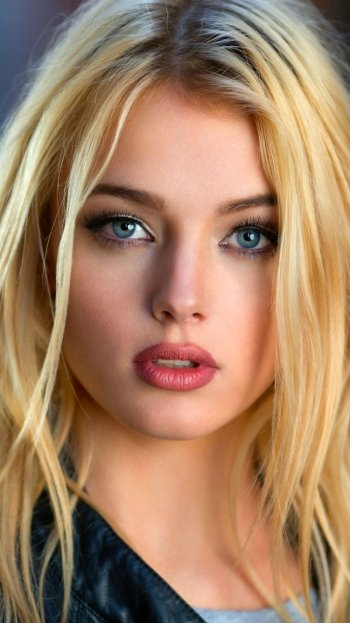 Close-up phone wallpaper of a blonde woman with striking blue eyes, neutral expression, and loose hair framing her face.