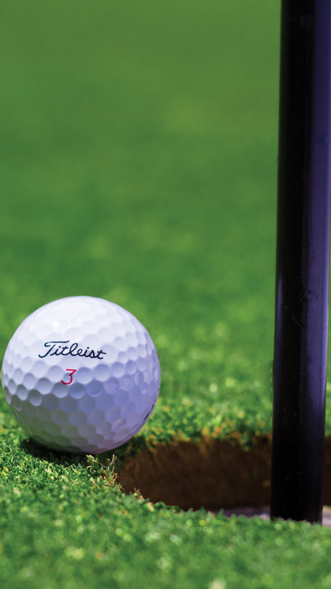 A Fitleist golf ball beside a hole on a golf course