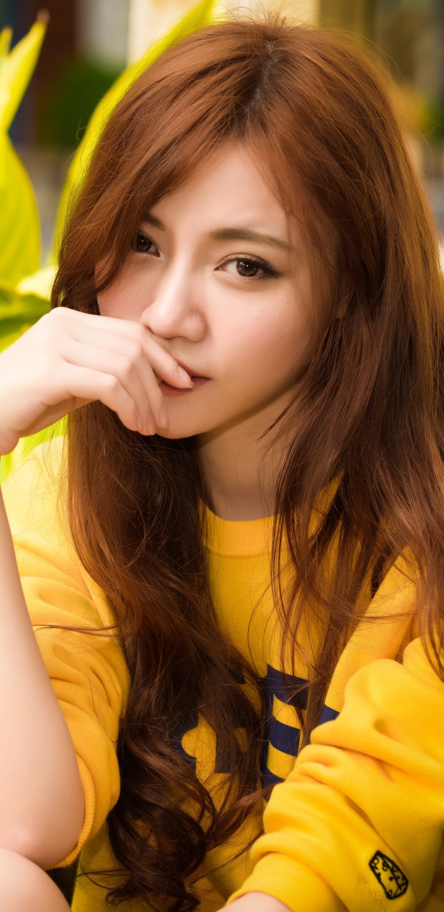 Portrait of an Asian redhead woman with brown eyes wearing a yellow sweatshirt, featured as a phone wallpaper for iPhones and Android devices.