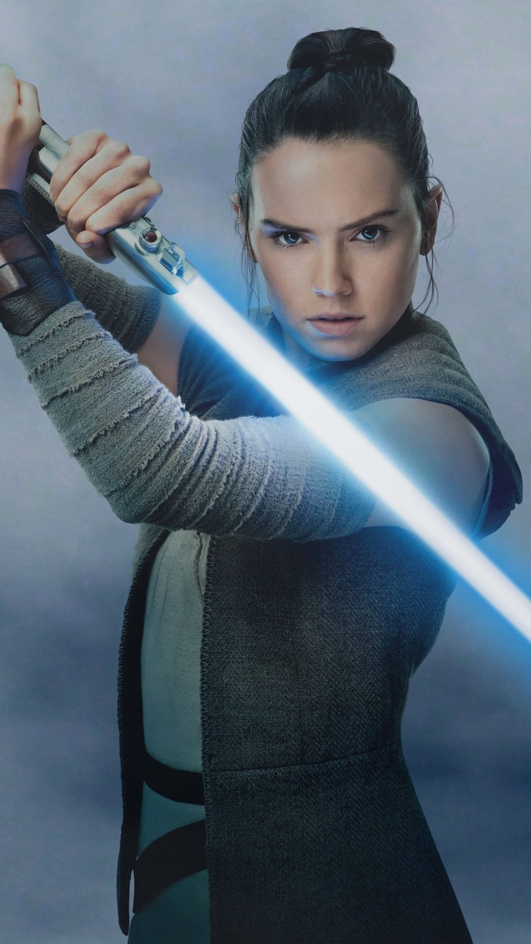 Phone wallpaper portrait of Rey (Star Wars) from the movie Star Wars: The Last Jedi, gripping a glowing blue lightsaber in a ready, focused stance.