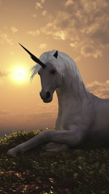 Fantasy phone wallpaper: a white unicorn reclining on a grassy hill, its horn silhouetted against a golden sunset.