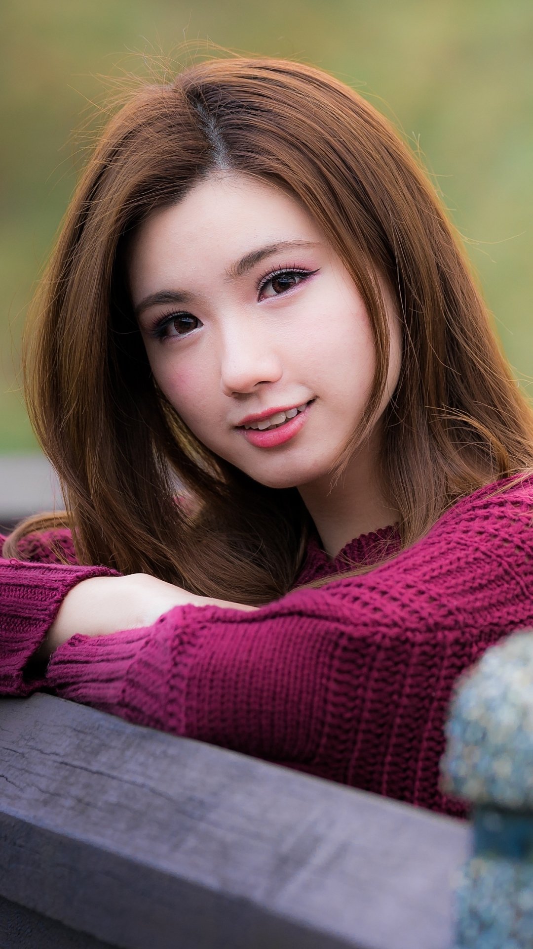 Portrait of a smiling Asian woman with red hair wearing a purple sweater, captured in a phone wallpaper format for iPhone and Android screens.