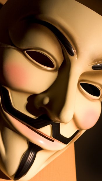 Phone wallpaper close-up of an Anonymous (Guy Fawkes) mask in warm light, symbolizing technology, anonymity, and hacker culture.
