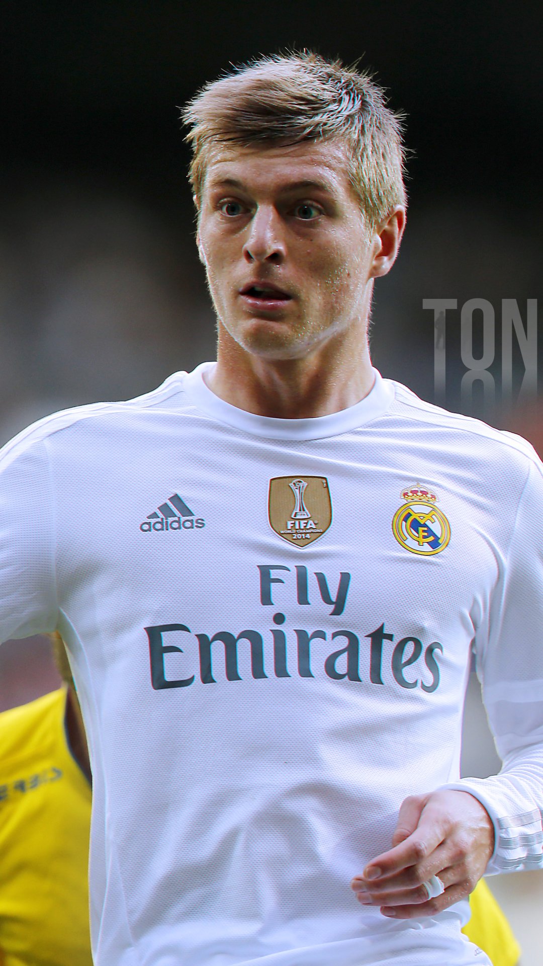 Phone wallpaper featuring Real Madrid midfielder Toni Kroos in the team’s white jersey with Fly Emirates logo, designed for both iPhone and Android screens.