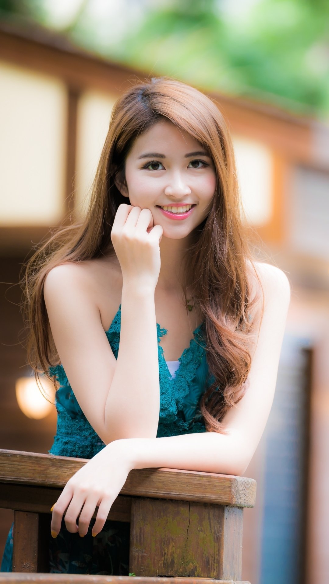 Portrait of a smiling Asian woman with long brunette hair, captured with depth of field, featured on a phone wallpaper compatible with iPhones and Android devices.