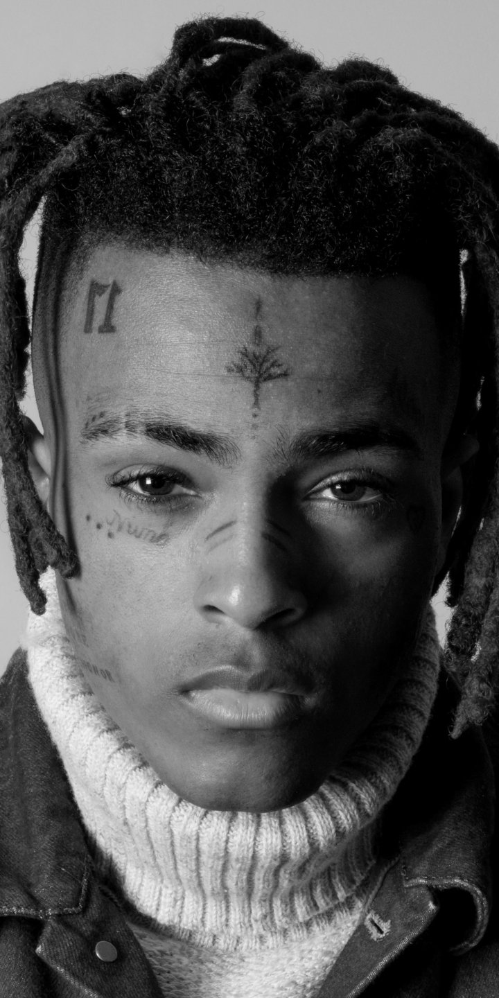 Black-and-white close-up portrait of XXXTentacion with facial tattoos, styled hair, and a turtleneck sweater phone wallpaper for iPhone and Android.
