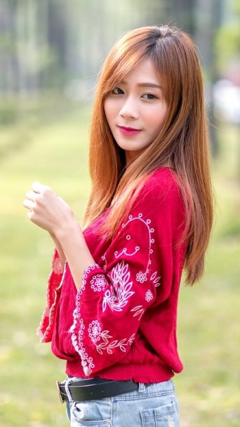 Phone wallpaper of a redheaded woman model with long hair in a red embroidered blouse, smiling softly at the camera outdoors.