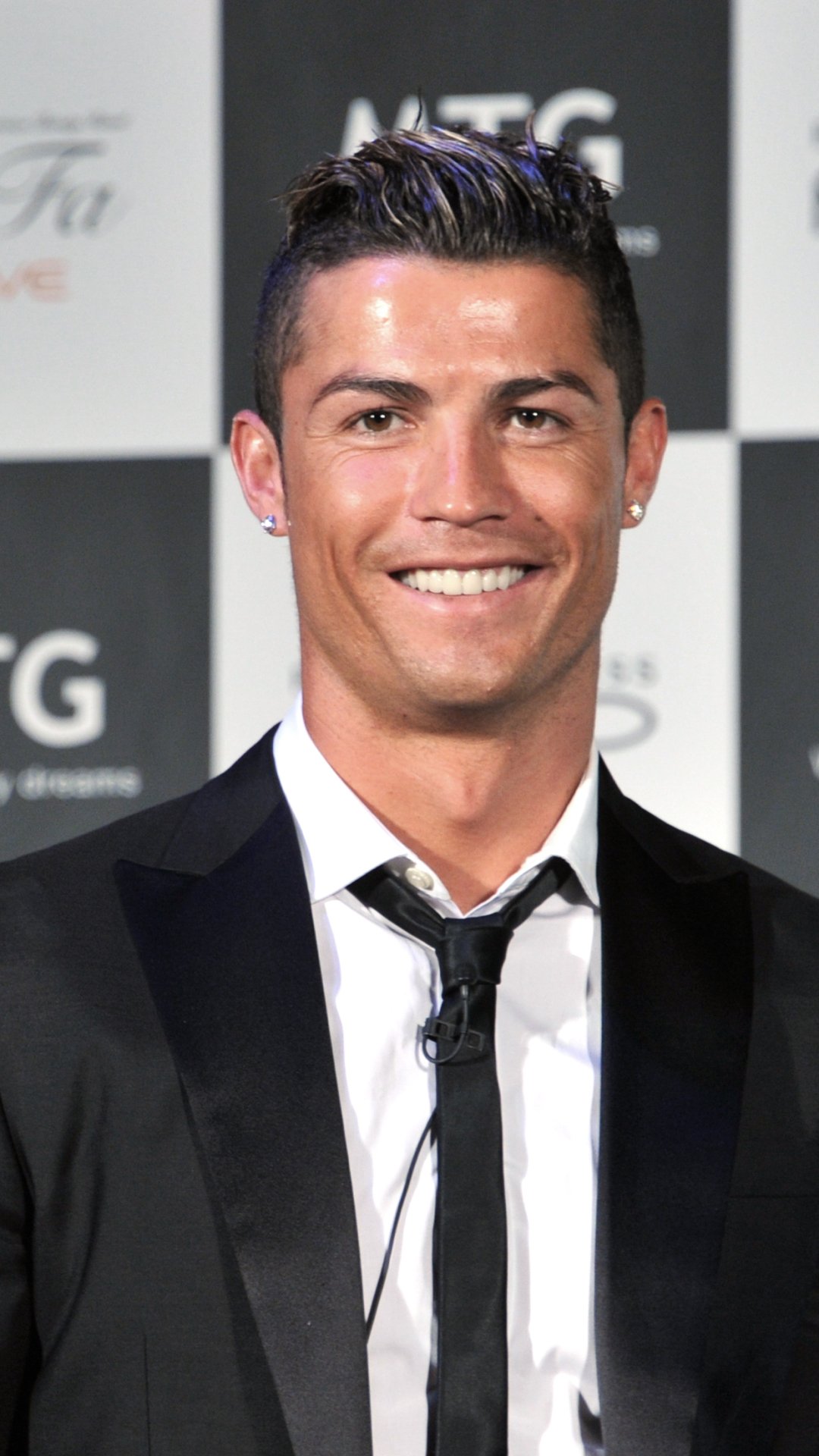 Phone wallpaper of a smiling Portuguese soccer player in a black suit and tie, posing against a sports sponsor backdrop.