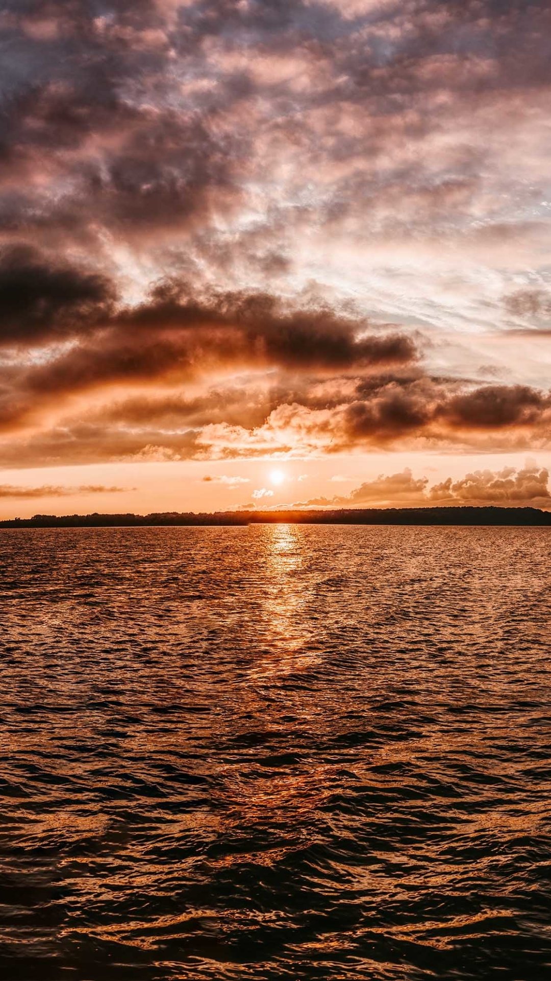 Phone wallpaper featuring ocean nature: a golden sunset reflecting on rippling water beneath a dramatic, cloud-streaked sky.