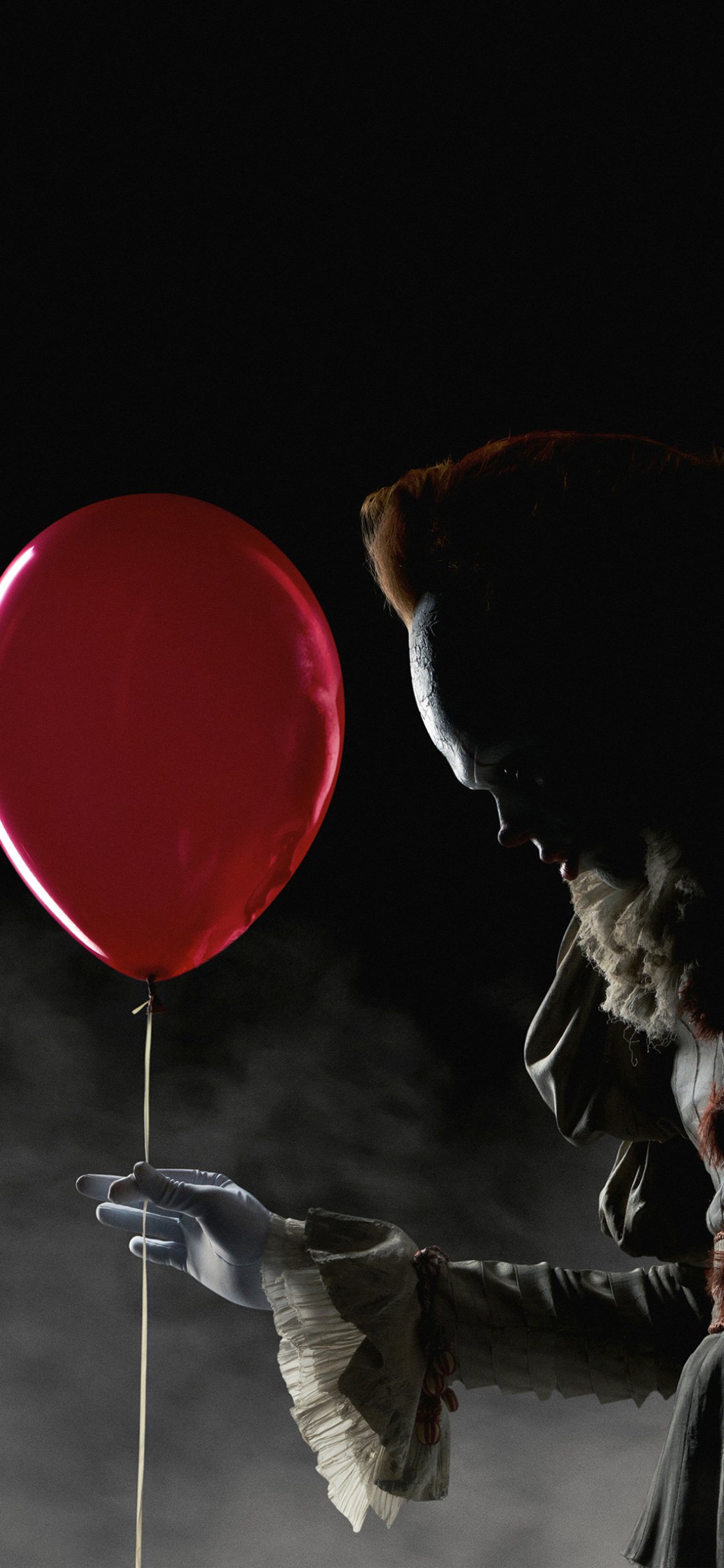 Phone wallpaper of Pennywise the clown from It (2017), shrouded in shadow holding a red balloon in fog — a scary horror movie portrait.