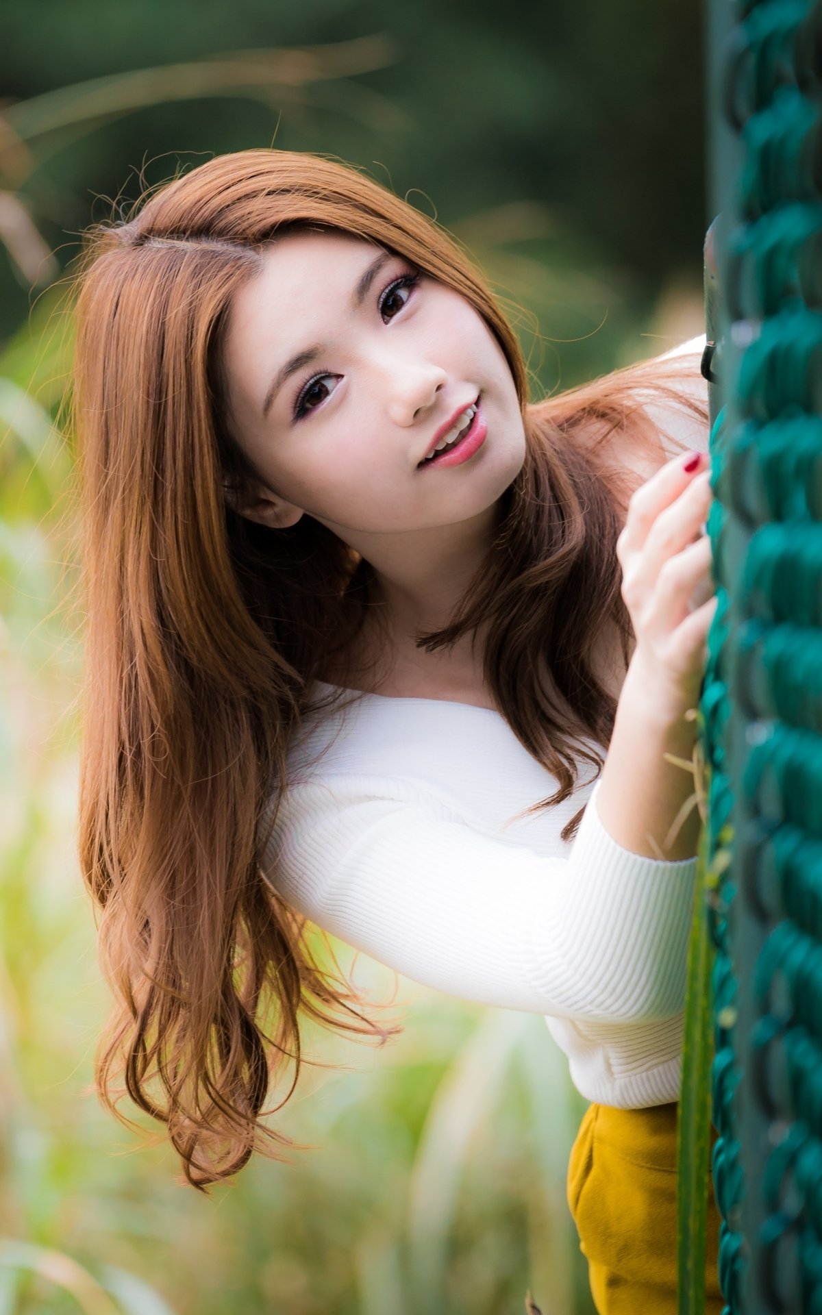 Portrait of a smiling Asian brunette woman with brown eyes, captured in a natural outdoor setting, designed as a phone wallpaper for iPhone and Android screens.
