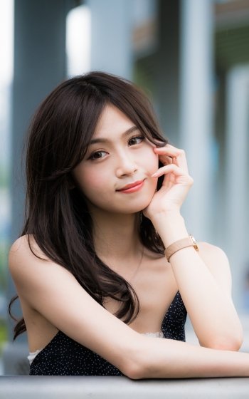 Brunette woman model smiling softly, resting her chin on her hand in a close-up portrait-style phone wallpaper.