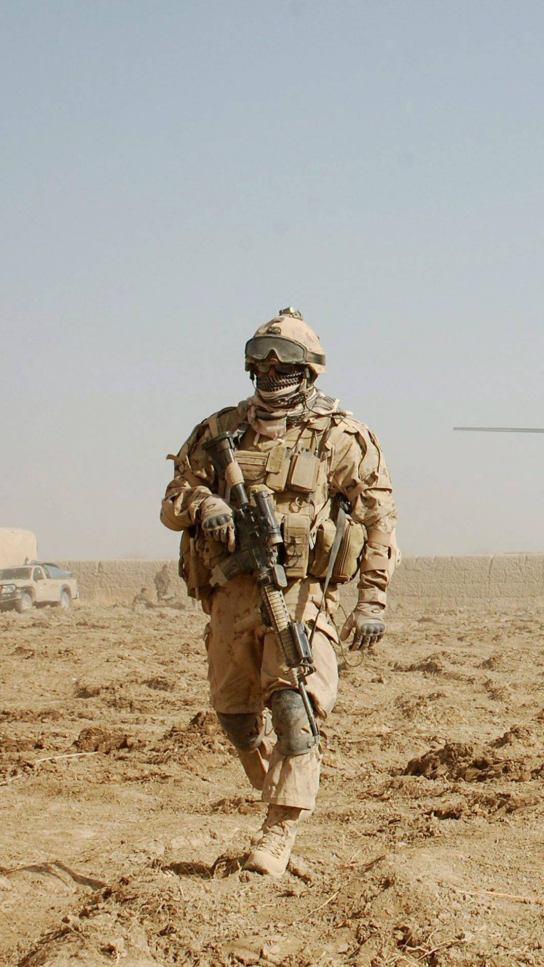 Phone wallpaper showing a military soldier in full desert combat gear walking across dry, sandy terrain under a pale sky.