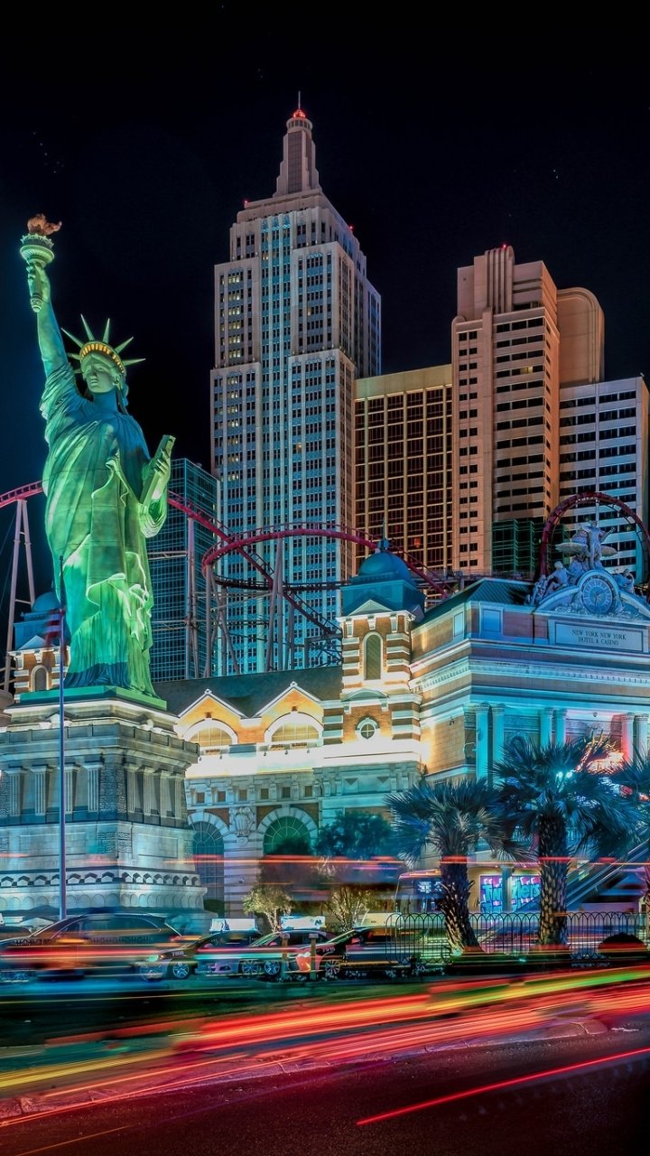 Time-lapse night shot of Las Vegas, USA: neon-lit skyscrapers, a replica Statue of Liberty and ornate casino buildings — vibrant man-made cityscape phone wallpaper.