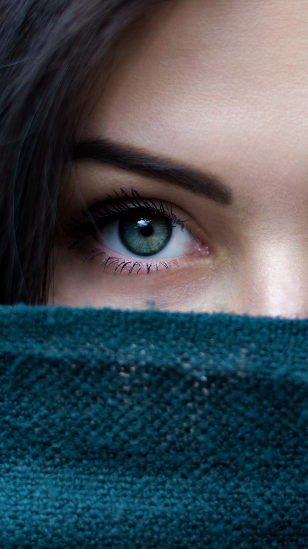 Close-up of a woman's face with a striking green eye peeking above a teal scarf, vertical phone wallpaper.