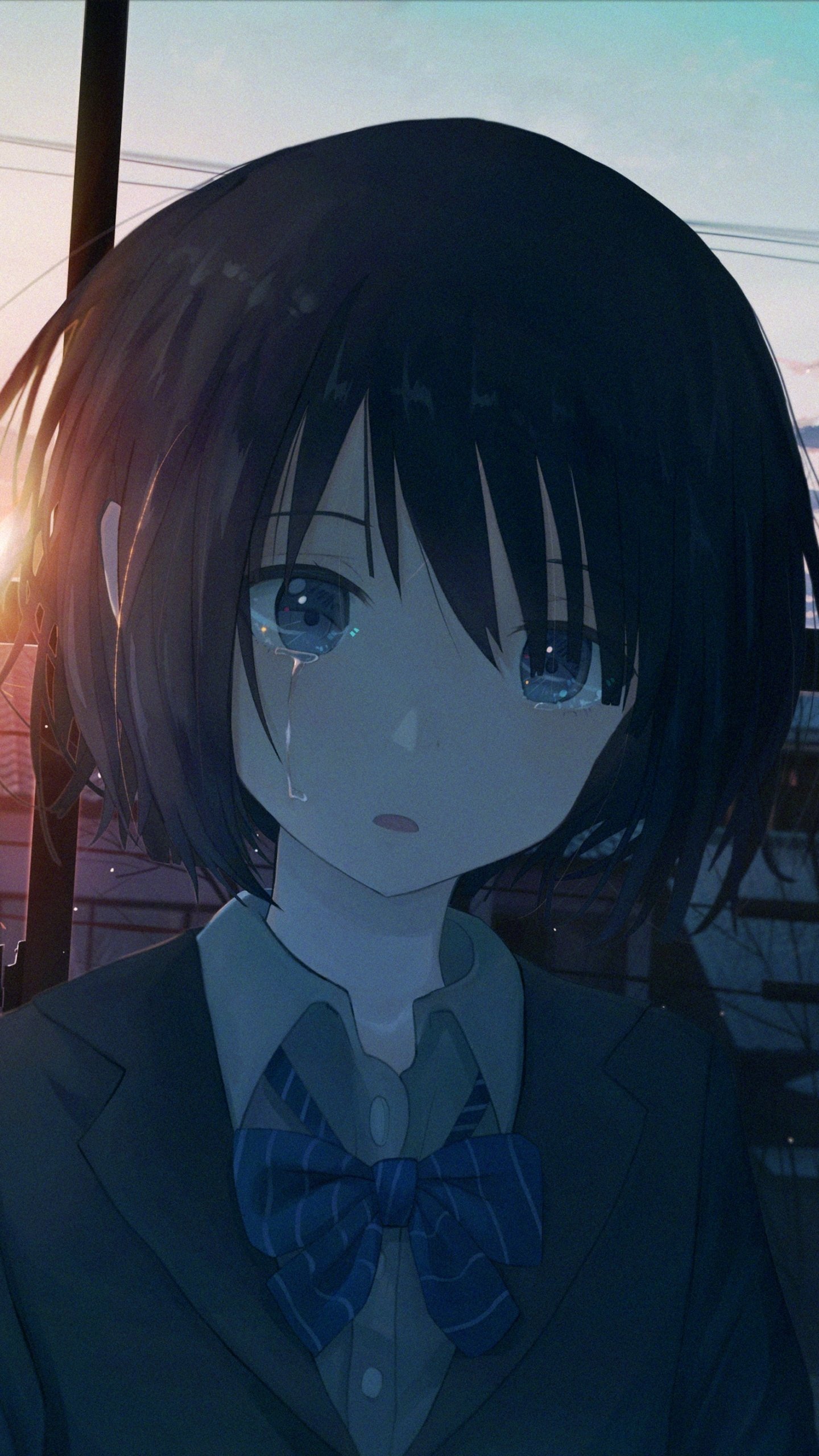 Phone wallpaper of an original anime girl with short dark hair and bow tie, tearful eyes against a glowing anime sunset and silhouetted rooftops.