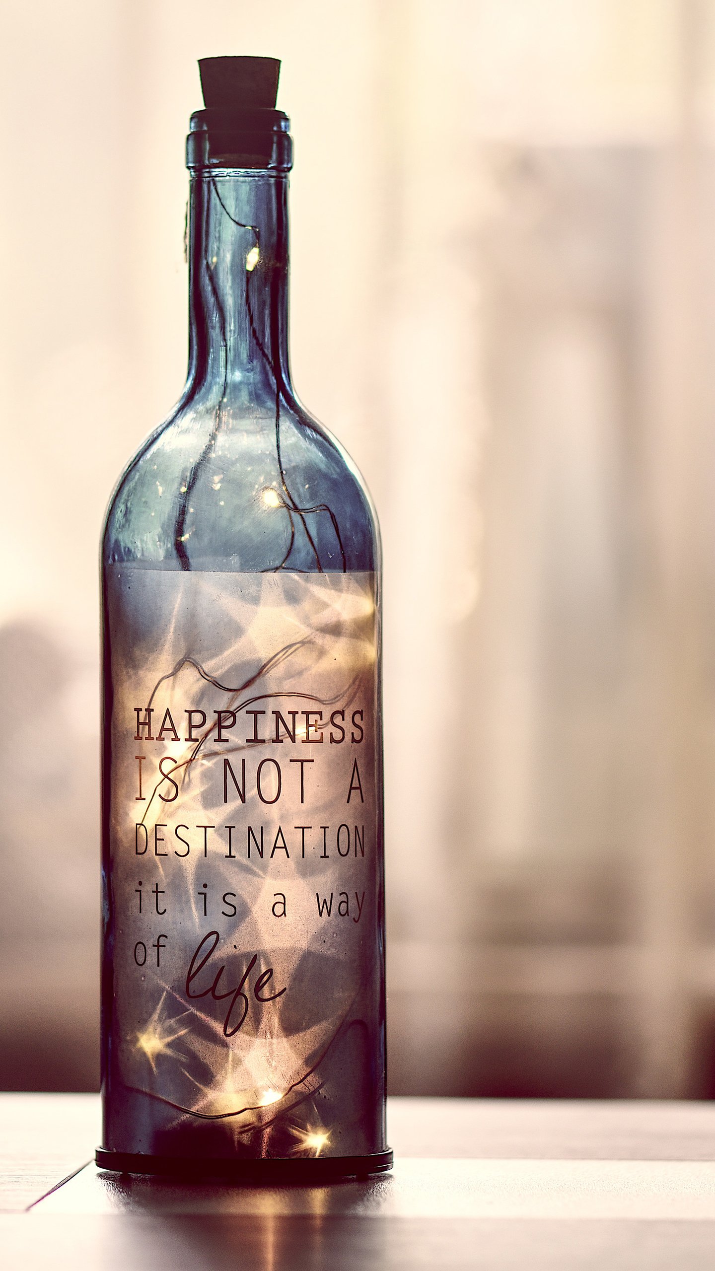 Phone wallpaper of a man-made glass bottle lit with fairy lights, bearing the statement Happiness is not a destination; it is a way of life.