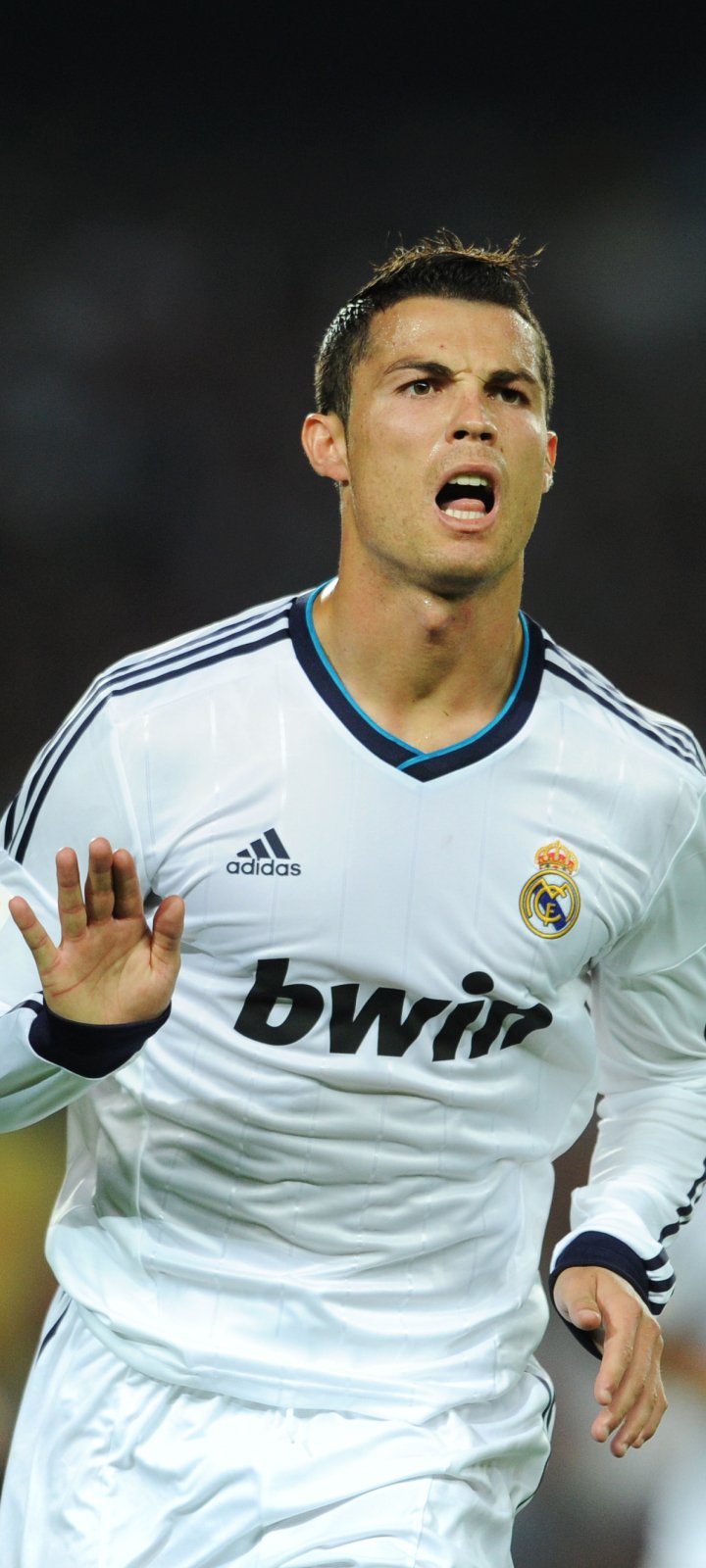 Phone wallpaper: close-up of a footballer in Real Madrid C.F. white kit, mouth open mid-shout, running with hand raised against a blurred stadium background.